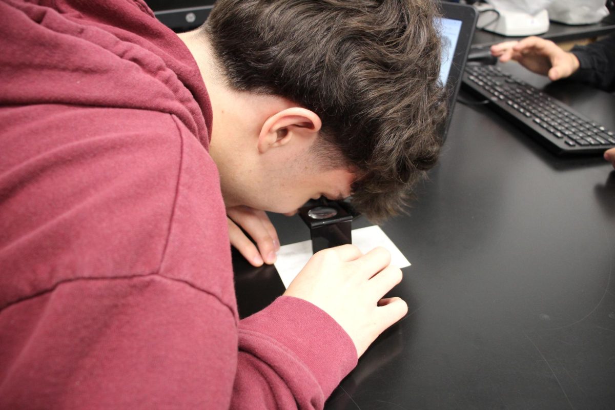 A student looking through a microscope to see a better look of a fingerprint.